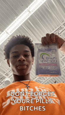 a man in an orange shirt holds up a package of pills