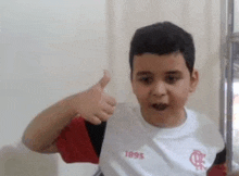 a young boy in a flamengo jersey is giving a thumbs up .