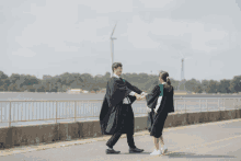 a man and woman in graduation gowns are holding hands in front of a windmill