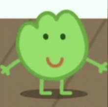 a green cartoon character with arms and legs is smiling and standing on a brown surface .