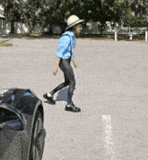 a man in a blue shirt and a white hat walks across a parking lot next to a black car