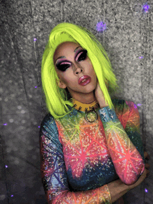 a drag queen with neon green hair and a rainbow top