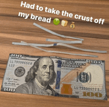 a 100 dollar bill sits on a wooden table next to bread and money