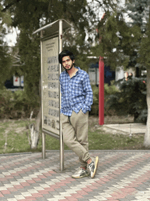 a man in a blue plaid shirt leans against a sign that says " a " on it