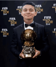 a man in a suit holds a trophy in front of a wall that says fifa ballon d' or