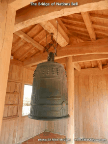 a large bell hangs from the ceiling of a wooden building with the words the bridge of nations bell above it