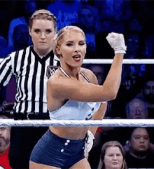 a woman is standing in a boxing ring with her fist in the air while a referee looks on .