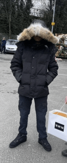 a man wearing a black jacket with a fur hood is standing in a parking lot