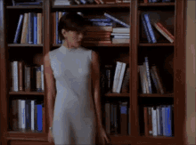 a woman in a white dress is standing in front of a bookshelf filled with books including one titled ' the bible '