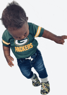 a baby wearing a green bay packers shirt and jeans