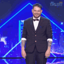 a man in a suit and bow tie stands on a stage in front of a sign that says all star talent