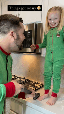 a little girl standing on a counter next to a man cleaning a stove