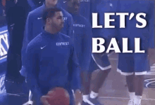 a man in a kentucky jersey is holding a basketball in front of a sign that says let 's ball