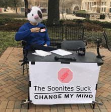 a man is sitting at a table with a sign that says the soonites suck change my mind