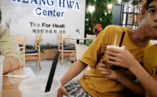 a man in a yellow shirt is sitting in front of a sign that says " tea for health "