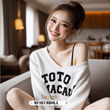 a woman wearing a toto macau sweater is sitting on a couch