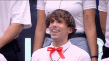 a man with curly hair wearing a red bow tie smiles