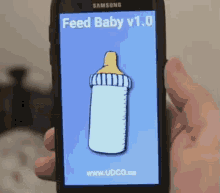 a person is holding a samsung phone with a feed baby v1.0 app on the screen