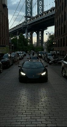 a black lamborghini is parked on a brick street with a bridge in the background