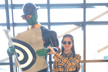 a woman standing next to a statue of a man with a target on his chest