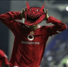 a man in a red vodafone shirt is wearing a red devil mask .