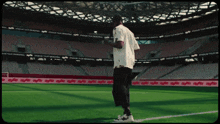 a man in a white shirt stands on a soccer field in front of a stadium that says stadium tour