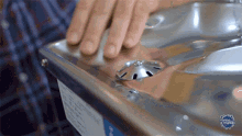 a close up of a person 's hand touching a stainless steel fountain with a label that says el mundo