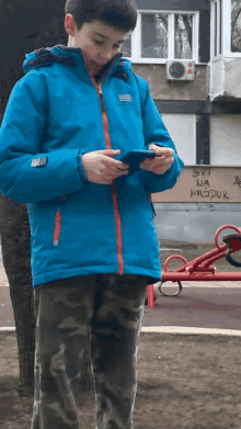 a boy in a blue jacket looks at a cell phone