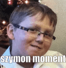 a young boy wearing glasses is sitting in front of a christmas tree and smiling .