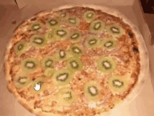 a pizza with kiwi slices on it is in a cardboard box