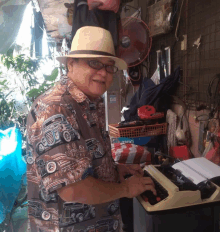 a man wearing a hat and glasses is typing on a typewriter