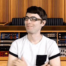 a man wearing glasses and a white shirt stands in front of a shelf with a bunch of equipment on it