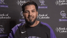 a man with a beard is smiling in front of a wall with bank of colorado logos on it .