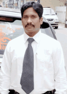 a man in a white shirt and tie is standing in front of a car with a license plate that says rj 5852