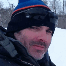 a man wearing a beanie and goggles is smiling in the snow