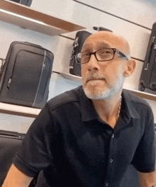 a bald man with glasses and a beard is sitting in front of suitcases