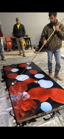 a man in a camo jacket is holding a stick in front of a painting