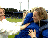 a woman in a blue jacket is hugging another woman in front of a stadium with a sign that says th