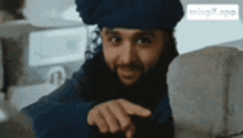 a man with a beard wearing a blue turban is pointing at the camera .