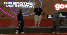 three men standing on a stage in front of a big brother vip kosova sign