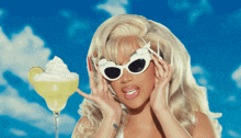 a blonde woman wearing sunglasses is holding a margarita