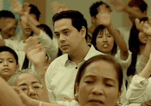 a man in a white shirt stands in a crowd of people raising their hands