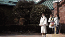 three women are standing in front of a brick building with a green roof and a sign that says ' e ' on it