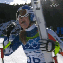 a woman wearing a blue helmet and goggles is holding a pair of skis with the number 16 on her chest