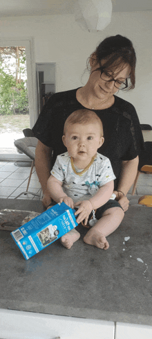 a woman is holding a baby who is holding a carton of milk