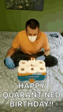 a man wearing a mask is sitting on a bed with a birthday cake made out of toilet paper .