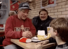 a group of men are sitting at a table in a fast food restaurant eating hamburgers and french fries .