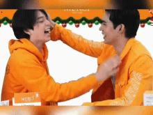 two men are laughing and hugging each other while wearing yellow hoodies .