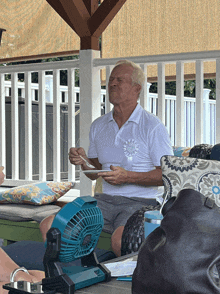 an older man sits on a porch with a fan