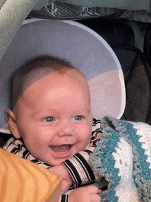 a baby is smiling while sitting in a stroller with a blanket